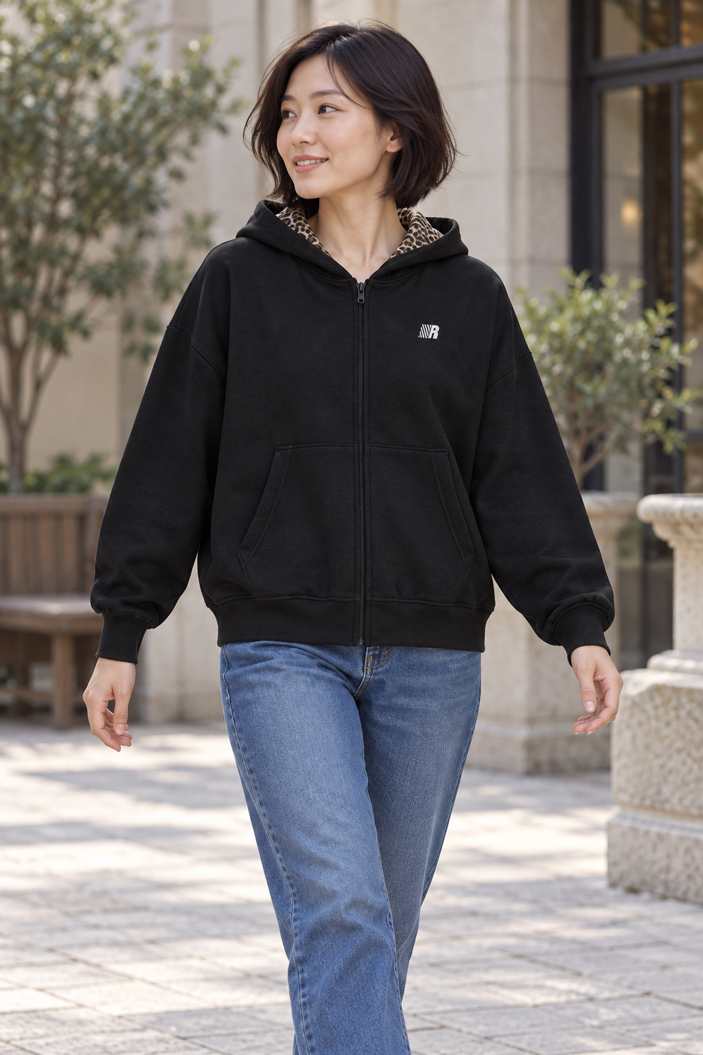 Women's black zip-front hooded cardigan jacket with chest emblem, outdoor lifestyle view.