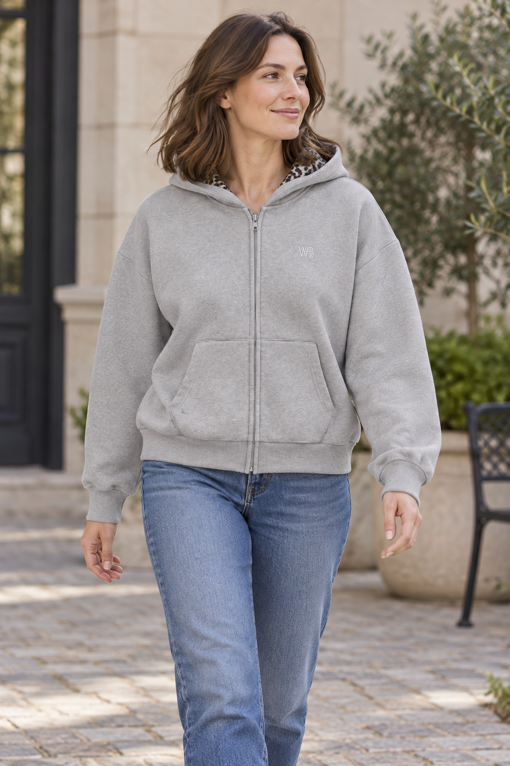 Women's floral gray zip-front hooded cardigan jacket with chest emblem, outdoor lifestyle view.