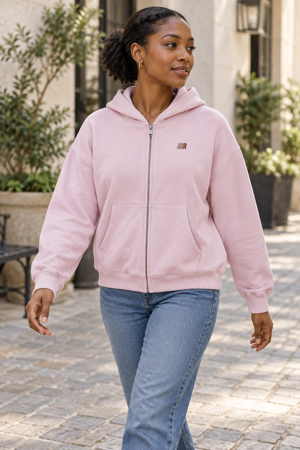 Women's pink zip-front hooded cardigan jacket with chest emblem, outdoor lifestyle view.
