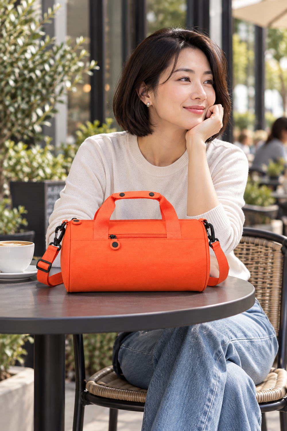 Orange Oxford travel shoulder bag on a café table beside a seated woman