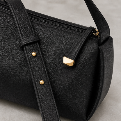 Close-up of black pebbled PU, top zipper, adjustable strap and gold-tone hardware